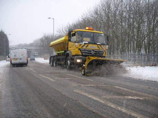 Large yellow snow plow truck clearing snowy road in wintry landscape.